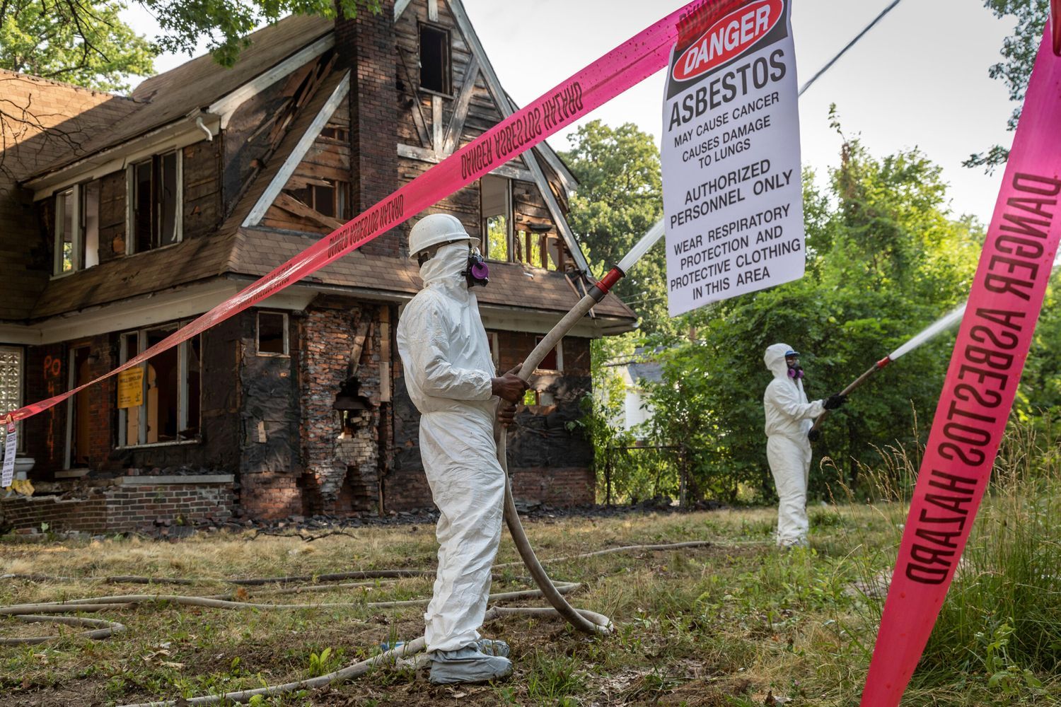A house taped off and being treated for asbestos by two people in full protective suits.