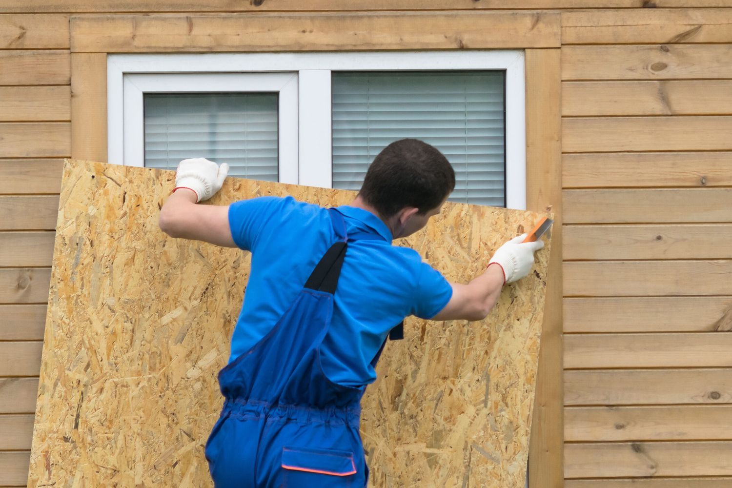 A man using plywood to board a window for hurricane season.