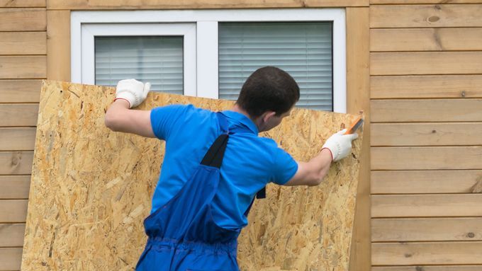 A man using plywood to board a window for hurricane season.