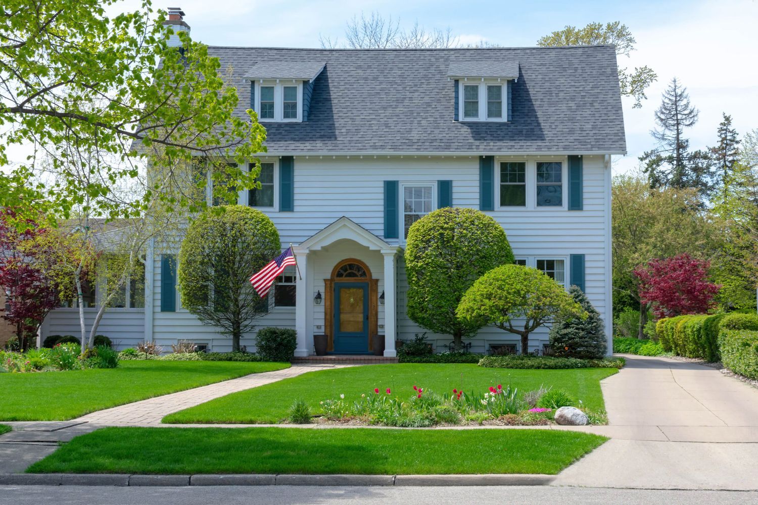 A two-story house with white siding, blue shutters, and a dark roof, that like any house should be tested for radon regularly.