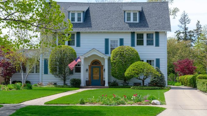 A two-story house with white siding, blue shutters, and a dark roof, that like any house should be tested for radon regularly.