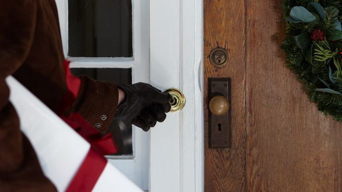 A man standing in front of a door, about to press a doorbell button.