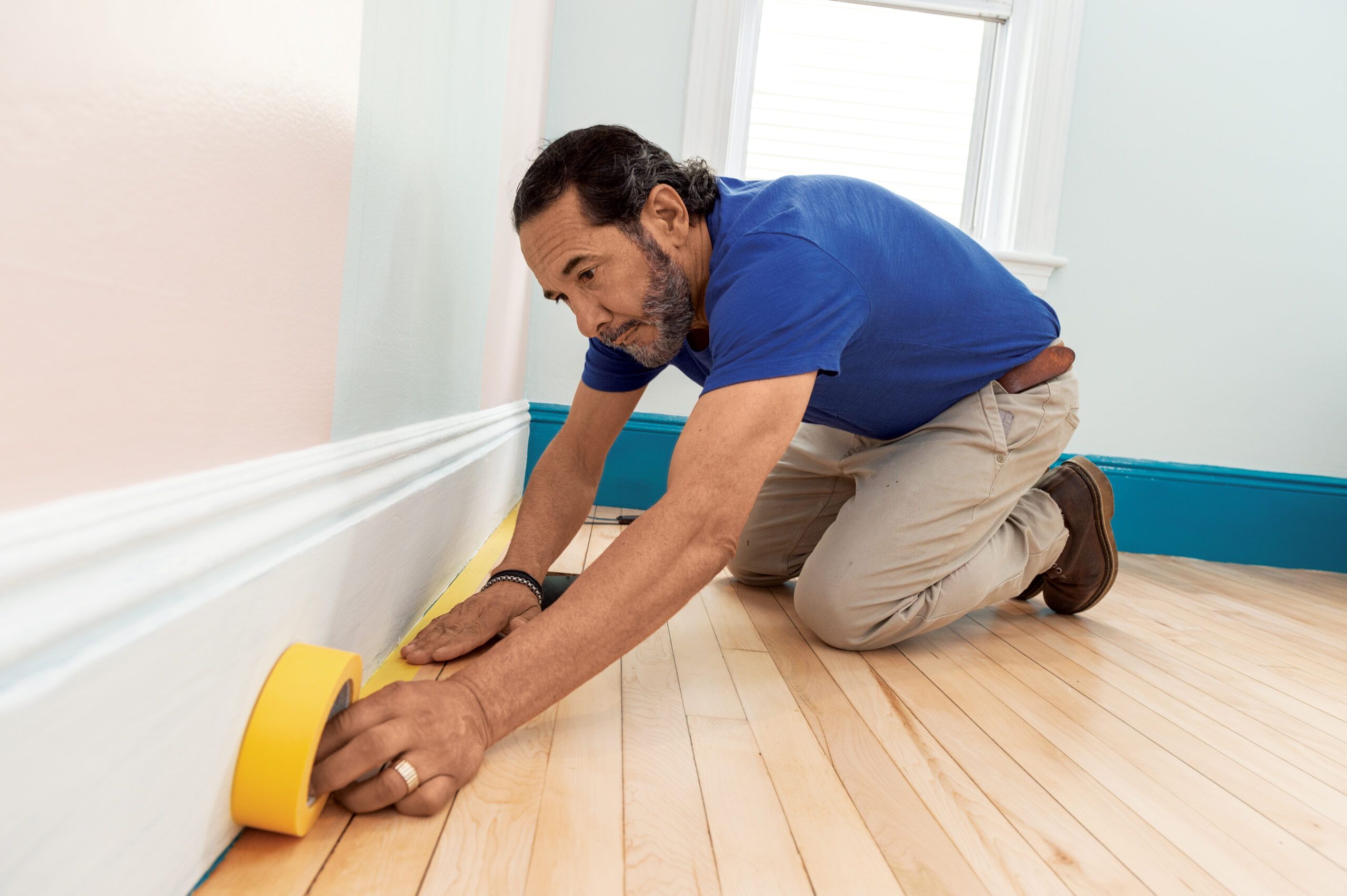 Mauro Henrique applying tape to the floor to prepare for a painting project.