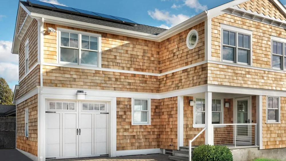 A 2 story home with yellow siding and an addition above the garage.