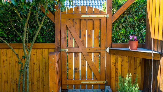 A stained wooden fence with a swinging door.