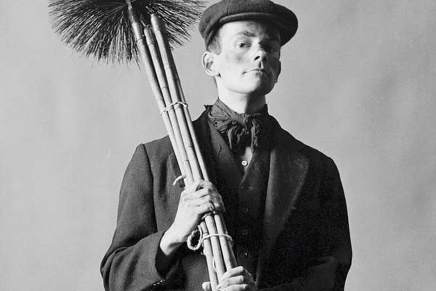 A black and white photo of a man holding a chimney cleaning tool.