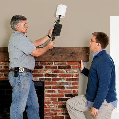 Tom Silva hangs lighting above a fireplace.