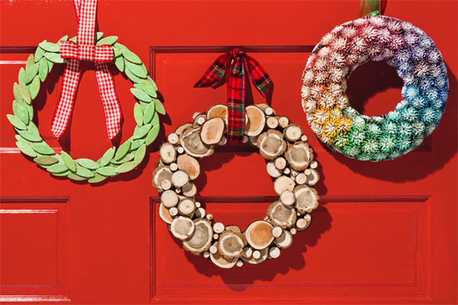 Three holiday wreaths against a red door.