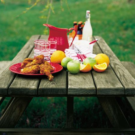 Picnic table with a water pitcher, fresh fruit, and fried chicken. 