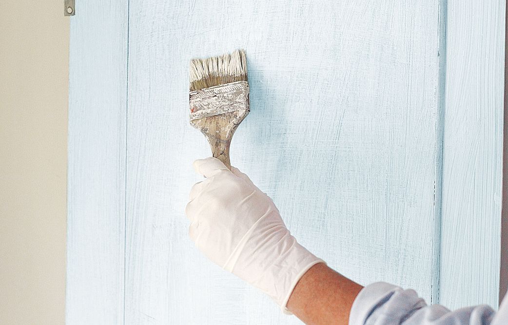 A person priming a cabinet for faux aging.