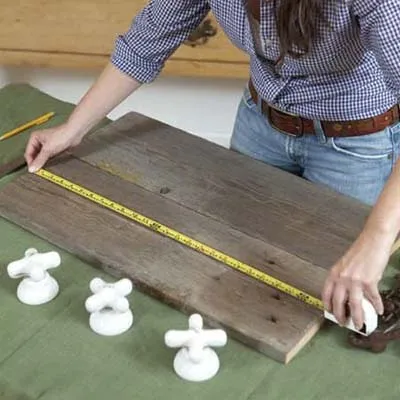 A woman measures a piece of wood to determine the spacing for the vintage taps for her towel rack.