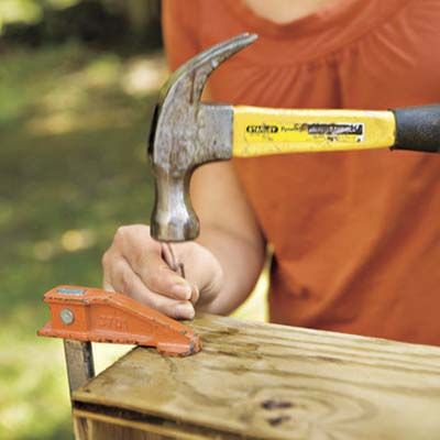 A man hammers a nail into a plywood frame.