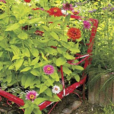 an old red metal bench with lots of plants and flowers