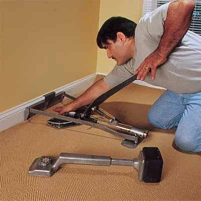A man uses a a lever-activated stretcher to install carpet.