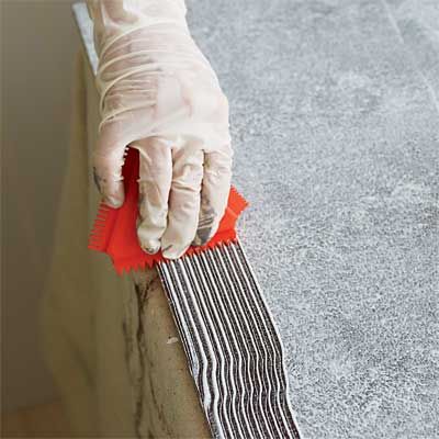 Image of a person using a paint comb to prepare the surface for using a grain rocker to create a faux wood grain effect. 