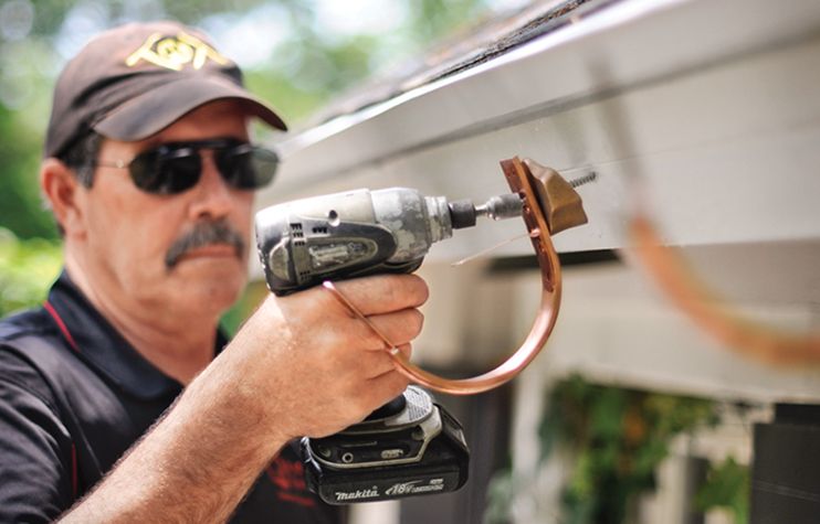 A man attaches gutter brackets in the process of installing a half-round gutter system.