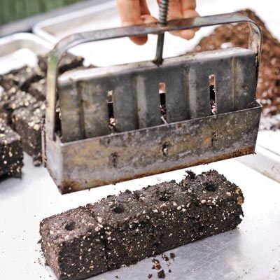 A soil block maker being lifted off a freshly pressed rectangular block of soil to start a plant or vegetable garden.