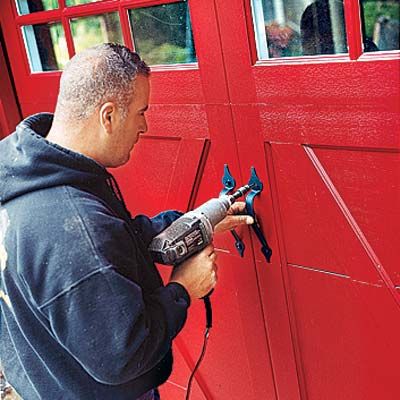 A person drills black metal handles onto a red garage door.