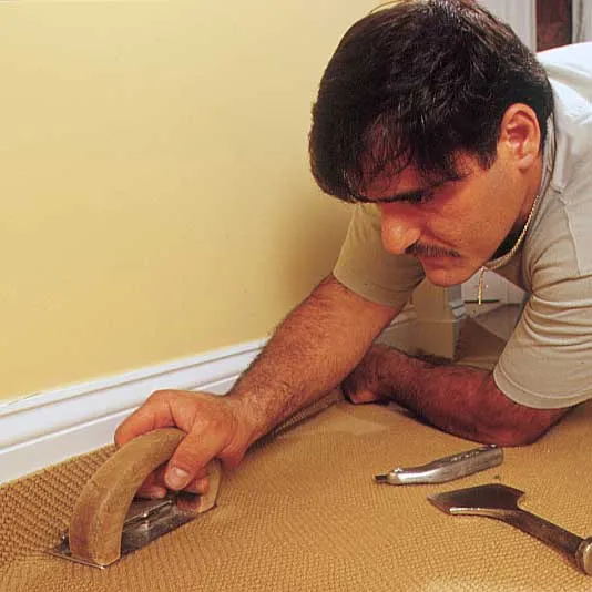 A man trims the excess carpet as he installs it.