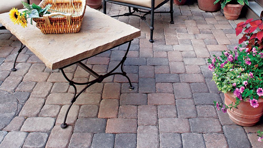 A DIY Stone Patio with a stone table, chairs, and plants on top of it.