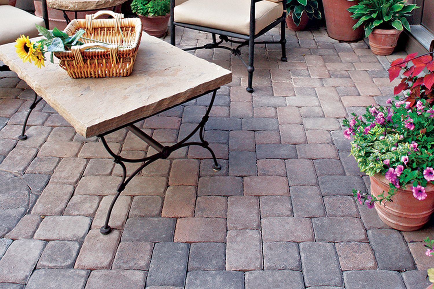 A DIY Stone Patio with a stone table, chairs, and plants on top of it.