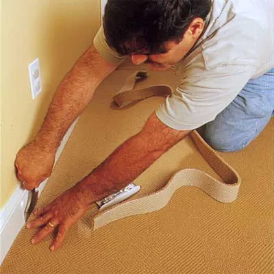 A man pushes the edges of the carpet under the baseboards.