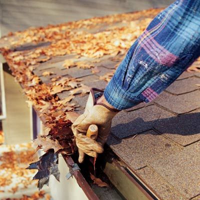 a person cleaning leaves out of a clogged gutter