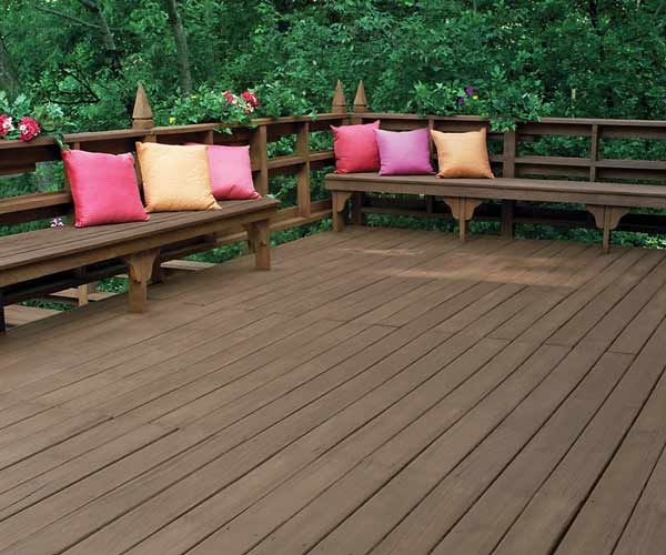 A stained wood deck with built in benches and pink and orange pillows.