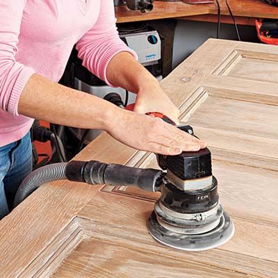 A person sands a wooden door to remove rough edges and splinters so it can be turned into a headboard.