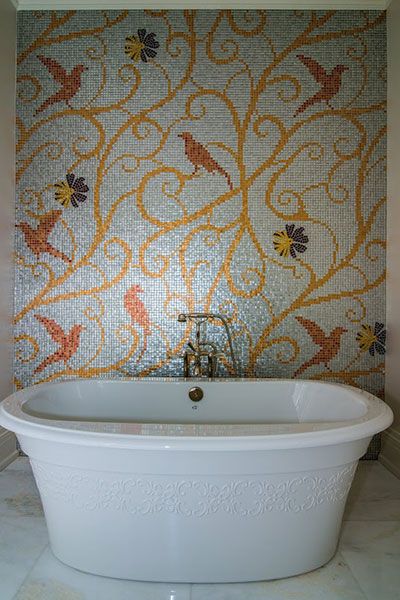 A bath tub in front of a tile wall with a floral design.