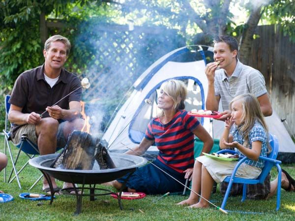 a camping party in a backyard with a tent, fire, and smores