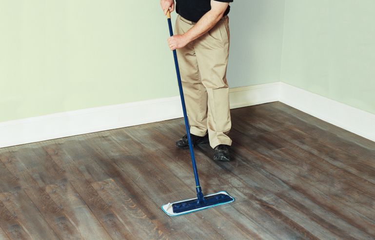 A man cleans up the leftover dust from the floor buffer before continuing to refinish the hardwood floors.