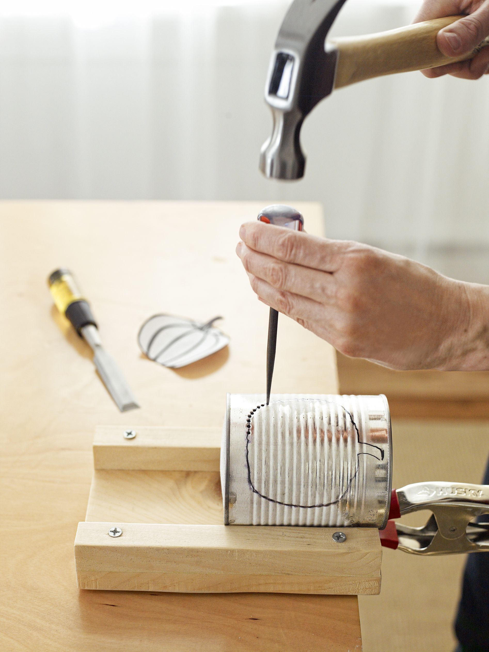 using a screwdriver and hammer to punch out the design on the tin can