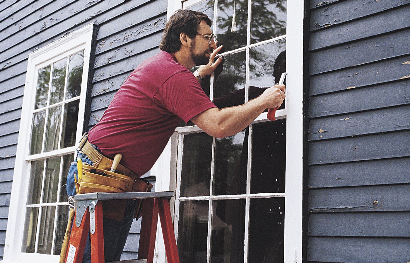 Norm Abram scraping trim paint from the wooden window off of the glass.