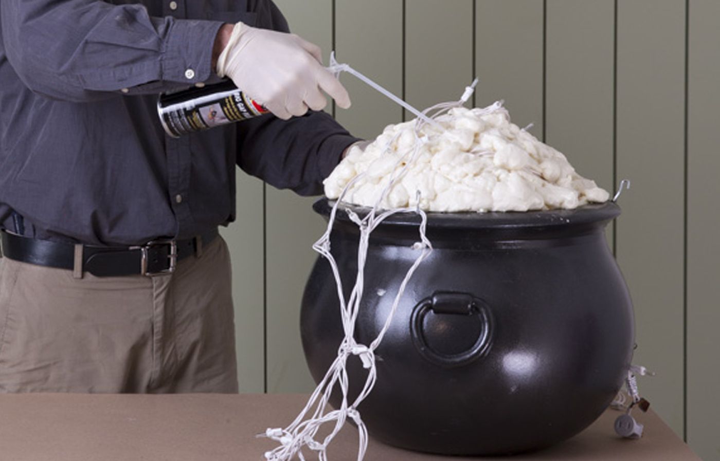 A man sprays foam in his witch's cauldron to give it a glowing brew effect.