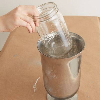 A glass vase with mercury colored paint drying on a table.