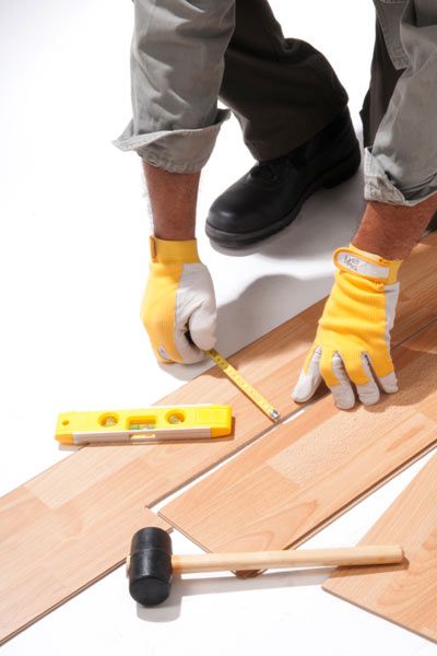 Prefinished wood floor boards being measured for width with a tape measure.