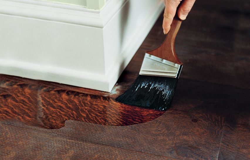 A person uses a paint brush to cut in along the floor edges with the new finish.