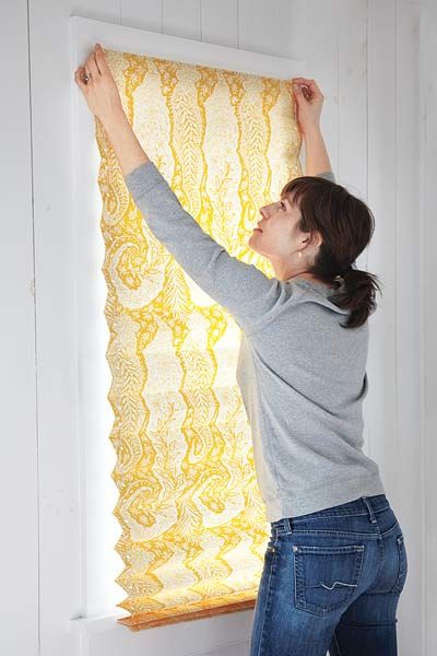 A woman hanging a privacy shade constructed from wallpaper scraps.