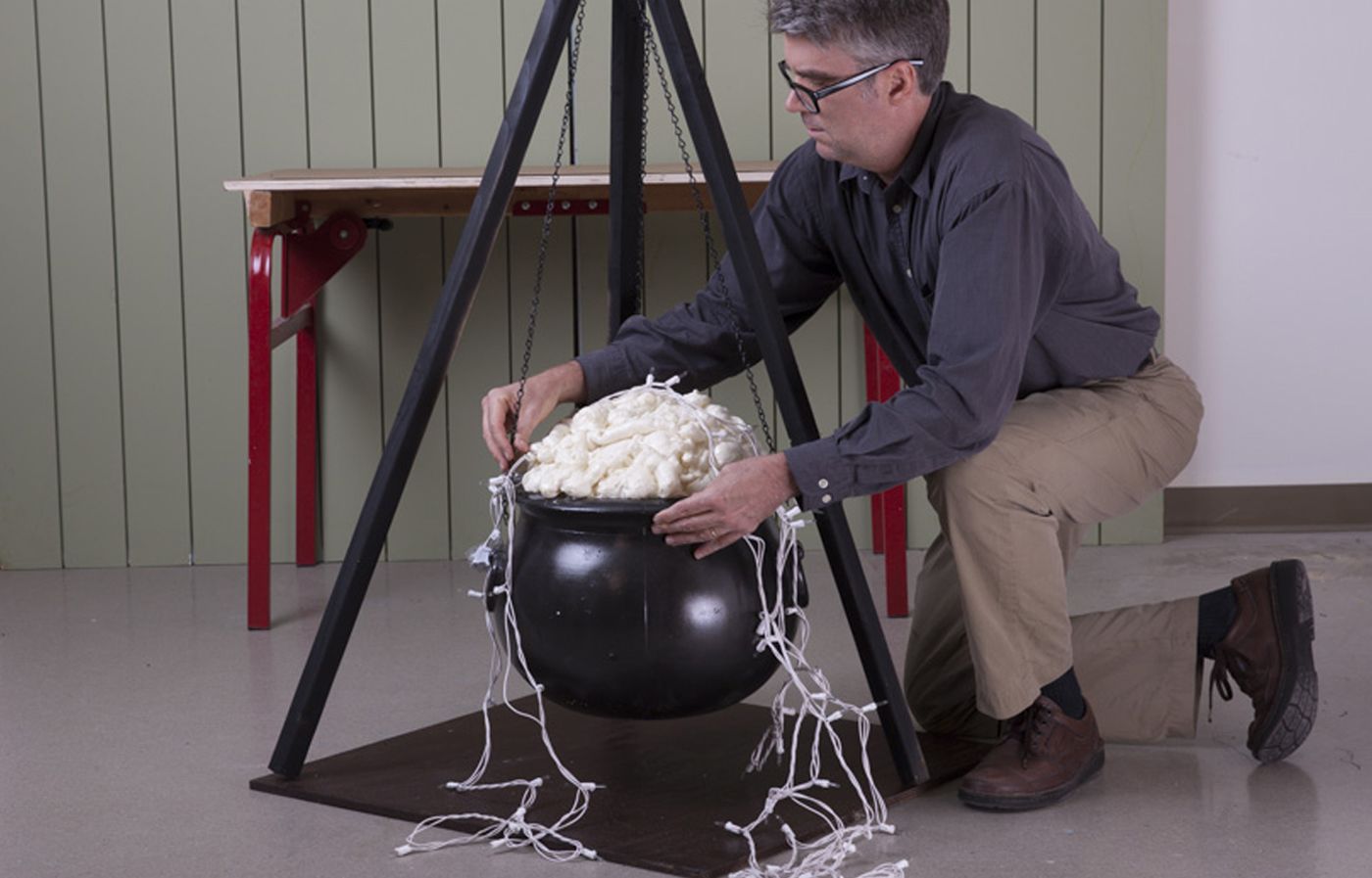 A man adds faux foam and bubbles to his Halloween witch's cauldron.