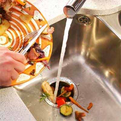 Someone scraping food off their plate into the garbage disposal, which could cause kitchen plumbing problems.