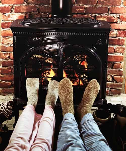 Two people warming their feet by a pellet stove.