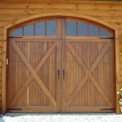 A wooden garage door with double doors, each having diagonal cross beams, a warm, natural finish and black hardware, including handles and hinges.