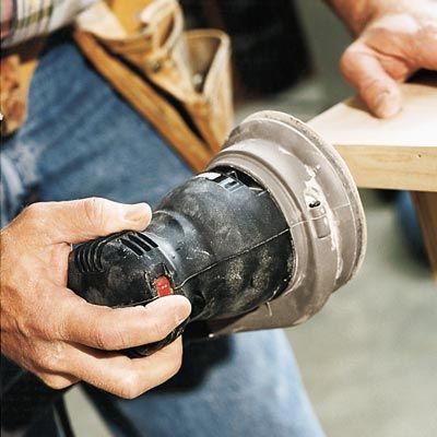 A random orbit sander being used to sand a corner of a piece of wood.