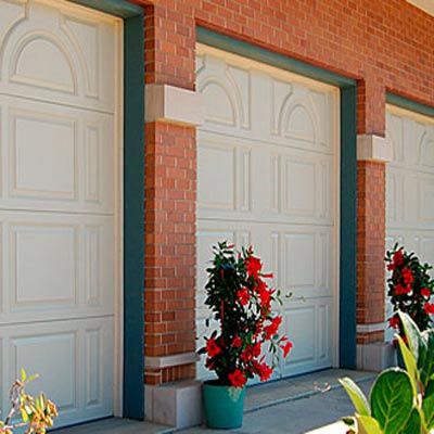 Cream colored fiberglass garage doors with decorative panels on a red brick house.