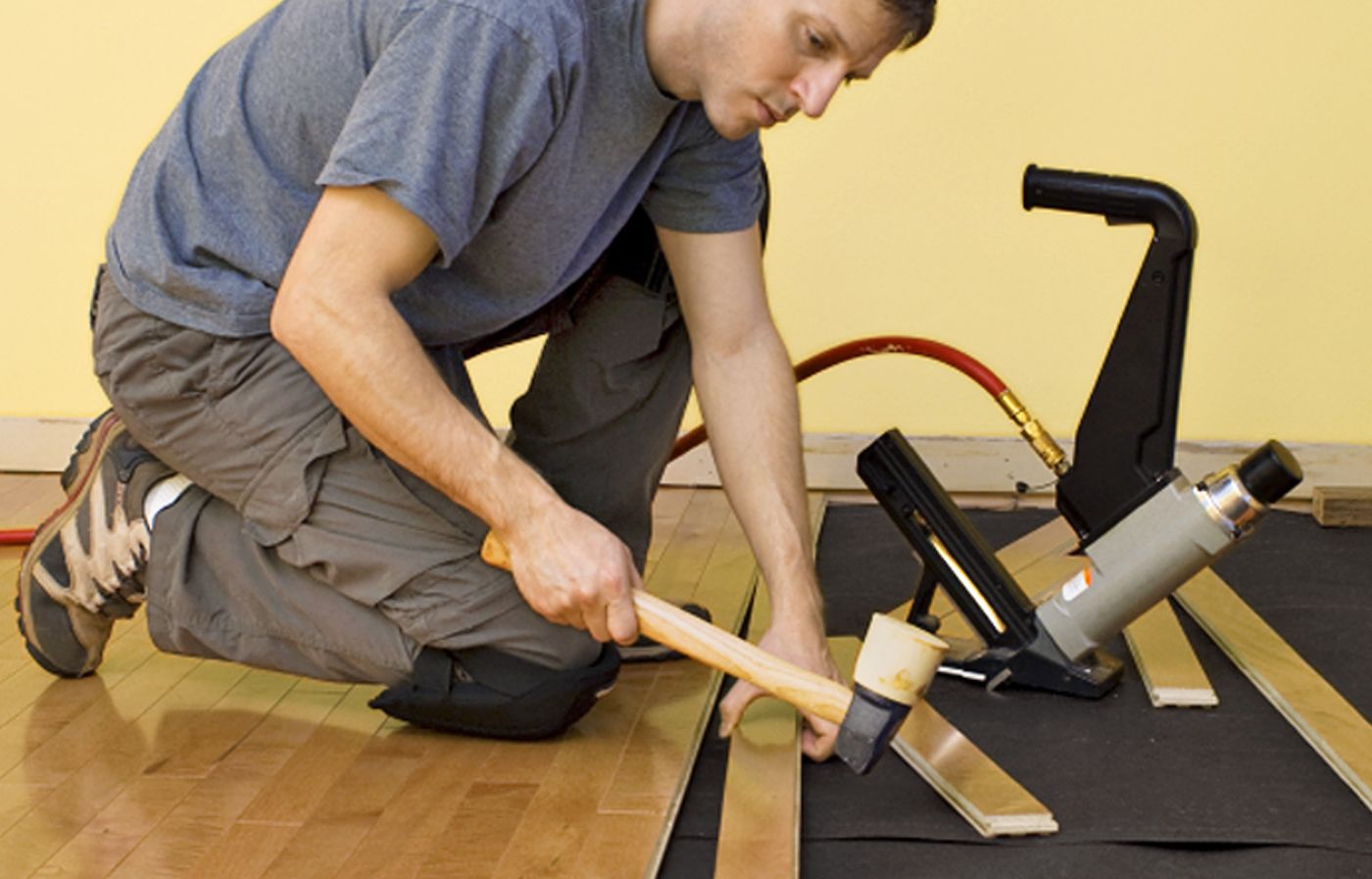 A man using a mallet to install bamboo flooring.