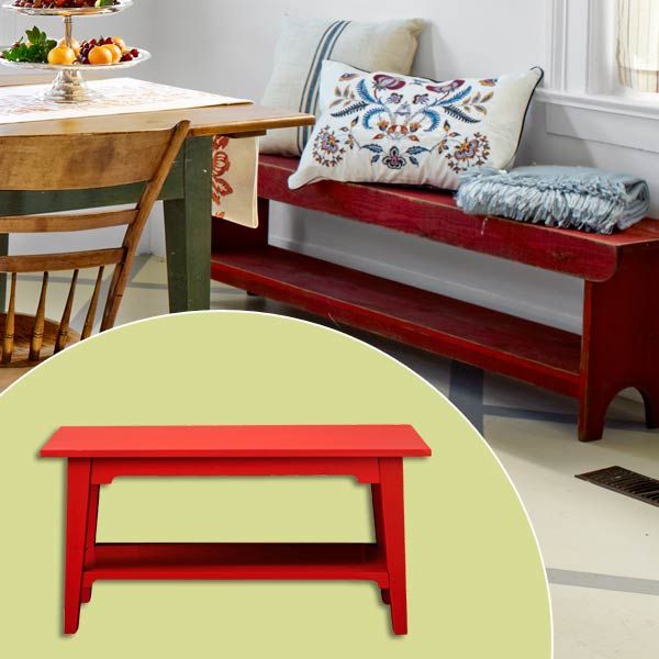 A rustic red bench with throw pillows sits against the wall in a dining room.