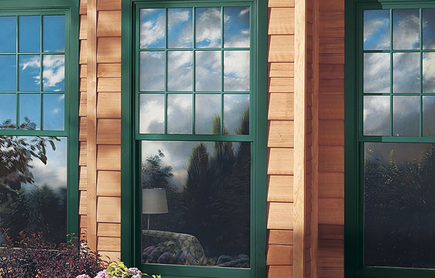 Three wooden windows painted green installed into a house with wooden siding.