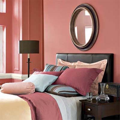 A bedroom with a pink painted wall and a circular wall mounted mirror.