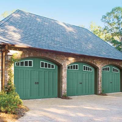 A house with three green garage doors with vertical paneling and decorative hardware.